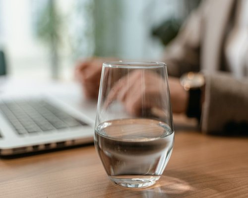 A fresh glass of filtered drinking water placed on a wooden desk next to a laptop in a Singapore home office